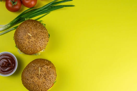 Two hamburgers close-up on a round wooden board, next to, tomatoes, chopped onions and spinach leaves.