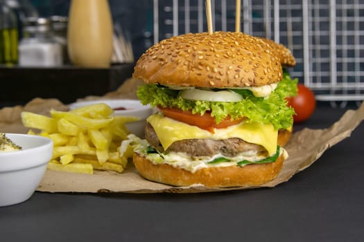 Close-up hamburger, sauces, french fries and tomatoes stand nearby, grill rack in the background.