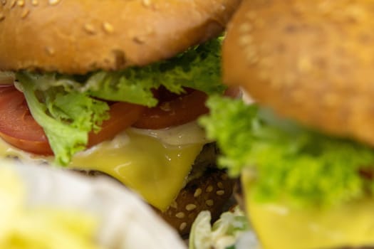 Two hamburgers close-up on a round wooden board, next to, tomatoes, chopped onions and spinach leaves.
