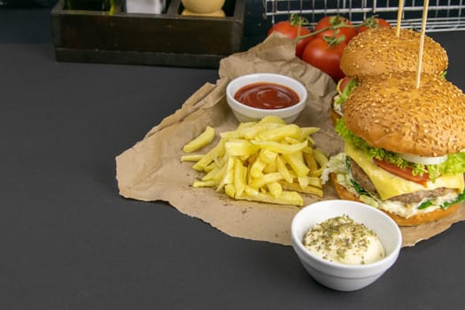 Close-up hamburger, sauces, french fries and tomatoes stand nearby, grill rack in the background.