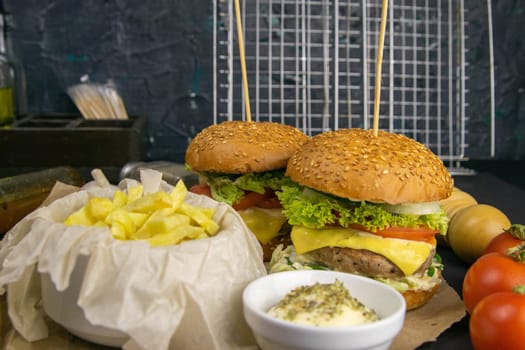 Two hamburgers close-up on a round wooden board, next to, tomatoes, chopped onions and spinach leaves.