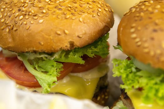 Two hamburgers close-up on a round wooden board, next to, tomatoes, chopped onions and spinach leaves.