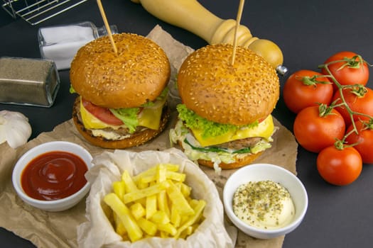 Two hamburgers close-up on a round wooden board, next to, tomatoes, chopped onions and spinach leaves.