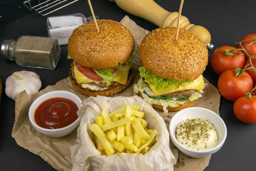 Two hamburgers close-up on a round wooden board, next to, tomatoes, chopped onions and spinach leaves.