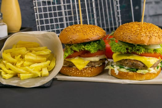 Close-up hamburger, sauces, french fries and tomatoes stand nearby, grill rack in the background.