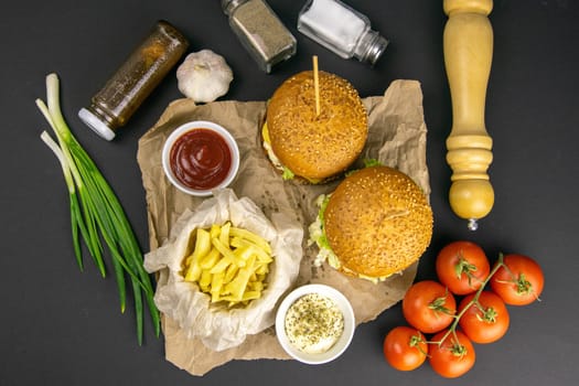 Close-up hamburger, sauces, french fries and tomatoes stand nearby, grill rack in the background.