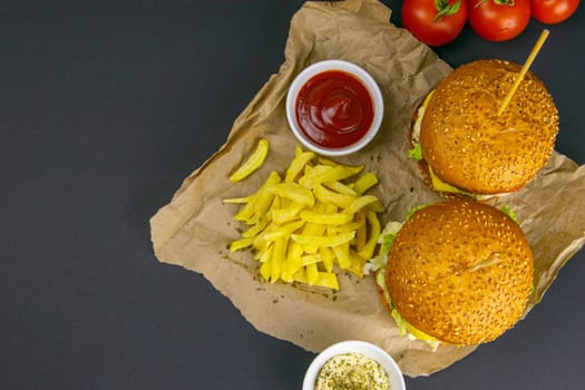Close-up hamburger, sauces, french fries and tomatoes stand nearby, grill rack in the background.