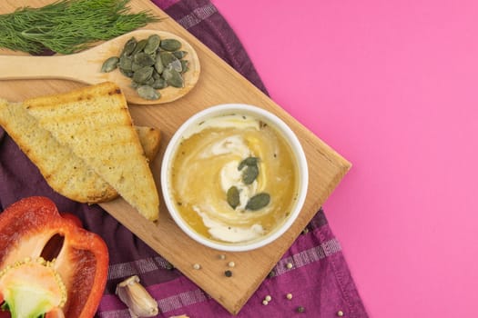 Pea soup with croutons stands on a green towel, next to there are tomatoes, toasts of pumpkin seeds, everything stands on the yellow table.