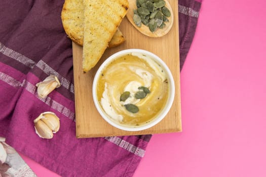Pea soup with croutons stands on a green towel, next to there are tomatoes, toasts of pumpkin seeds, everything stands on the yellow table.