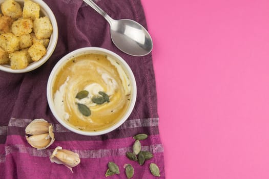 Pea soup with croutons stands on a green towel, next to there are tomatoes, toasts of pumpkin seeds, everything stands on the yellow table.