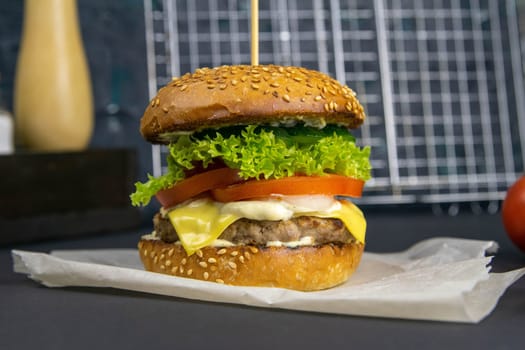 Close-up hamburger, sauces, french fries and tomatoes stand nearby, grill rack in the background.