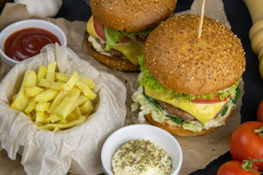 Two hamburgers close-up on a round wooden board, next to, tomatoes, chopped onions and spinach leaves.