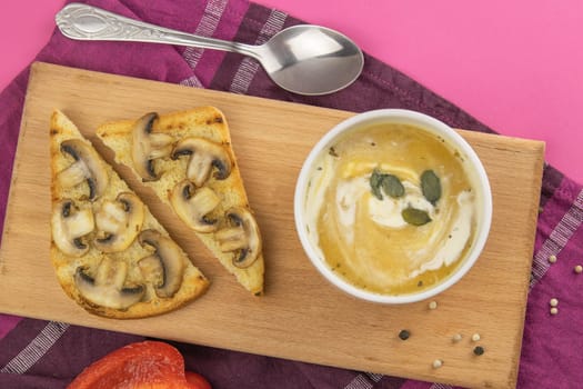 Pea soup with croutons stands on a green towel, next to there are tomatoes, toasts of pumpkin seeds, everything stands on the yellow table.