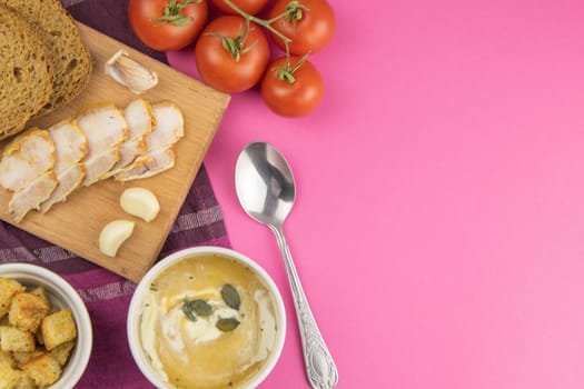 Pea soup with croutons stands on a green towel, next to there are tomatoes, toasts of pumpkin seeds, everything stands on the yellow table.