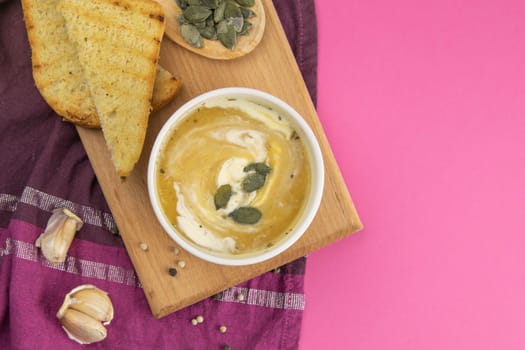 Pea soup with croutons stands on a green towel, next to there are tomatoes, toasts of pumpkin seeds, everything stands on the yellow table.