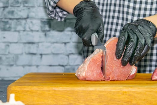 Female hands in black gloves cut juicy slices of pork, garlic stands nearby.