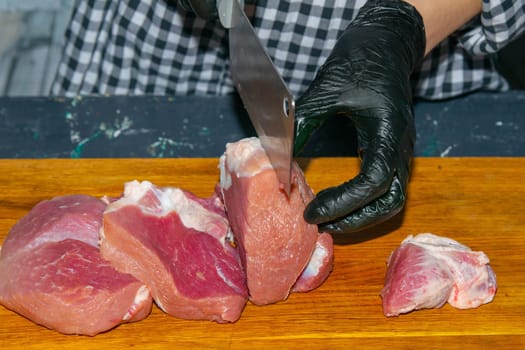 Female hands in black gloves cut juicy slices of pork, garlic stands nearby.