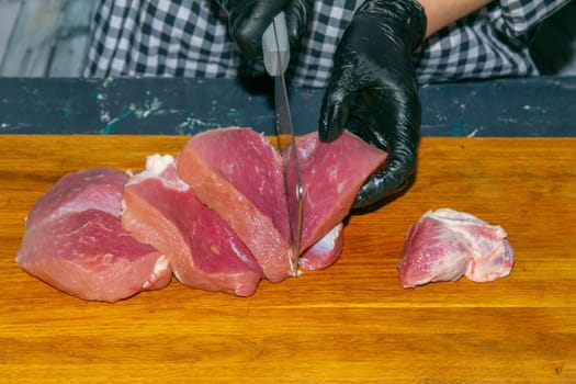 Female hands in black gloves cut juicy slices of pork, garlic stands nearby.