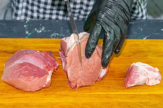 Female hands in black gloves cut juicy slices of pork, garlic stands nearby.