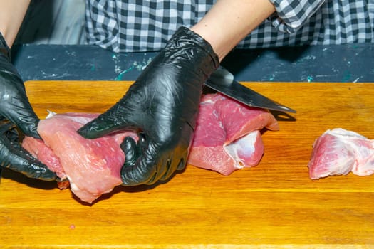 Female hands in black gloves cut juicy slices of pork, garlic stands nearby.