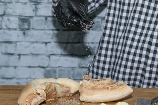 Female hands in black gloves cut juicy slices of pork, garlic stands nearby.