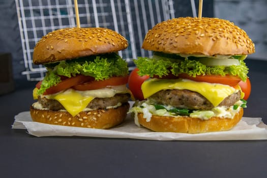 Close-up hamburger, sauces, french fries and tomatoes stand nearby, grill rack in the background.