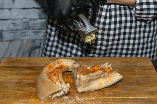 Female hands in black gloves cut juicy slices of pork, garlic stands nearby.