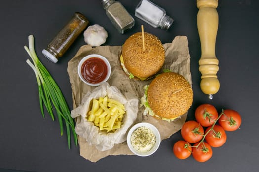 Close-up hamburger, sauces, french fries and tomatoes stand nearby, grill rack in the background.