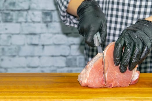Female hands in black gloves cut juicy slices of pork, garlic stands nearby.