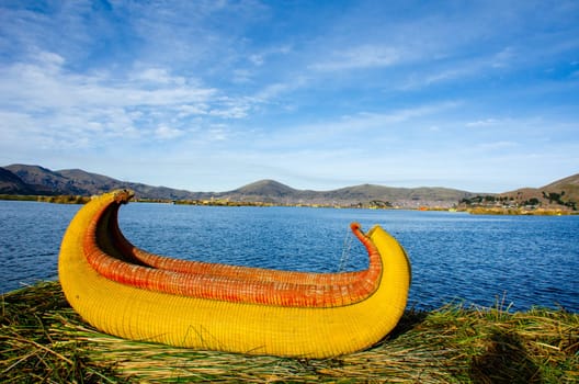 A reed canoe on the banks of the Uros Islands at Lake Titicaca. Puno, Peru on the far bank.