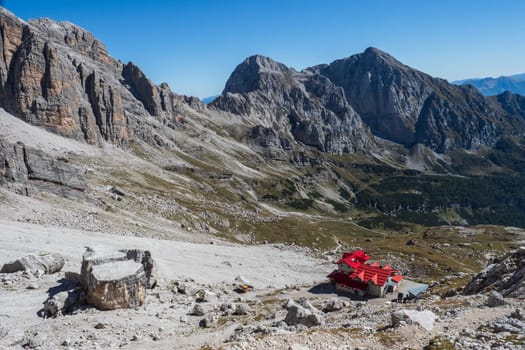Tourist with hiking backpacks in mountain hike on summer day. Man traveler hiking in beautiful mountain landscape. Climber and alpine hut in Dolomites Alps, Italy. g