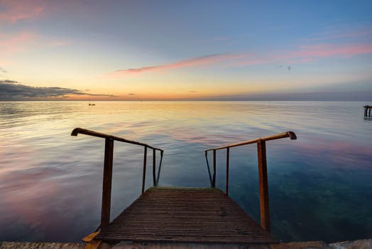 The old mittal staircase on the pier descends into the sea, against the background of the evening beautiful sunset