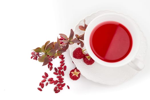 Healthy fruit tea with barberries and raspberries in white cup and branch of berberry isolated on white background. Top view