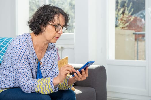 cheerful brunette senior woman using smartphone while sitting on a sofa