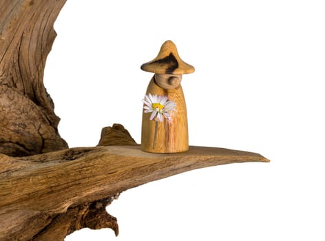 Turned wood gnome with a daisy in hand stands on an old tree stump isolated on white