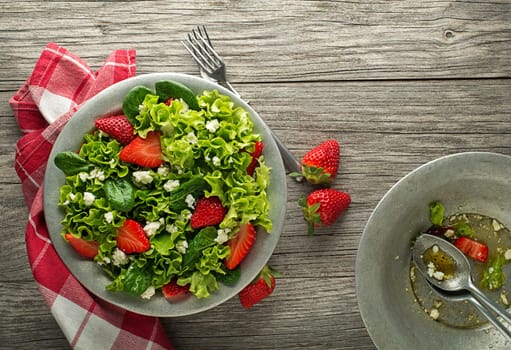 Healthy green salad with strawberry and fresh cheese on wooden table background. Healthy salad meal.
