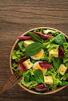 Healthy lettuce salad with eggs and cheese on wooden table background. Healthy meal.