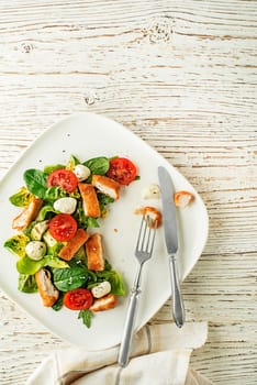 Healthy green salad with crispy fried breaded chicken breast strips and mozzarella on white background