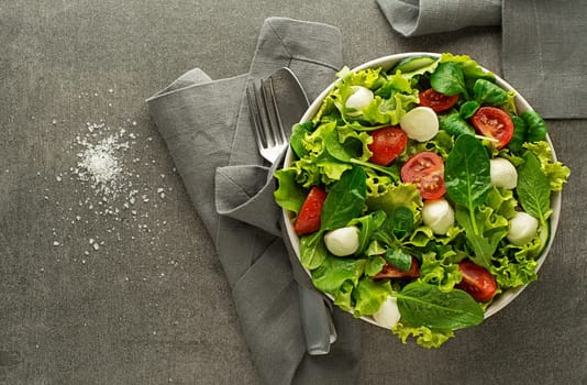 Healthy Green lettuce salad with tomato and mozzarella on grey table background