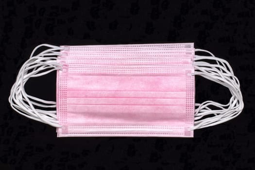 Coronavirus outbreak. Close-up of a stack of pink surgical masks or protective face mask on black background. Global pandemic concept. Macro photograph of medical face masks with copy space.