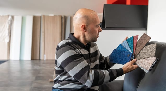 The man selects a new cover for the sofa from the color card sampler.