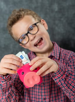 funny young boy with glasses puts money into a piggy bank