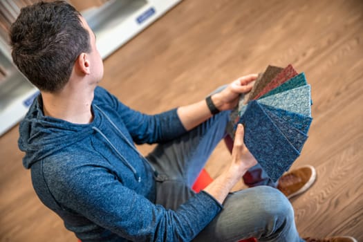 the man chooses the color of the new carpet according to the pattern book in the flooring shop.