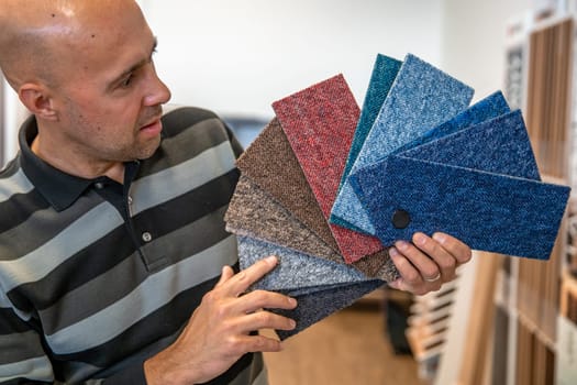 the man chooses the color of the new carpet according to the pattern book in the flooring shop.
