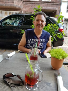 LÜNEBURG, NIEDERSACHSEN, GERMANY - JULI 27, 2018:.Man is sitting in the beer garden of a restaurant in Lueneburg with mobile phone in hand. Looking at the camera.