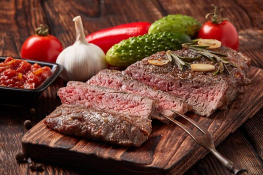 Grilled meat. Medium rare beef steak on wooden cutting board, rosemary twigs, spices and vegatables on brown wooden background. Steak menu