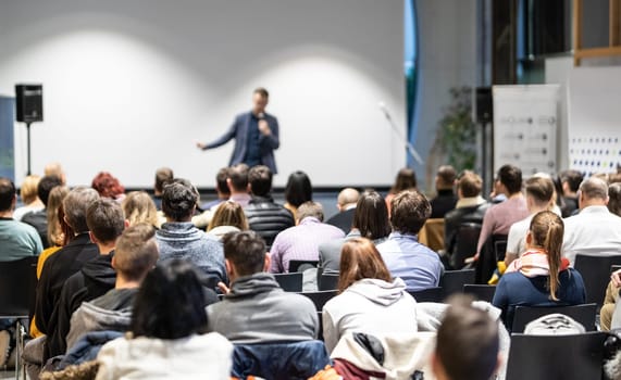 Speaker giving a talk in conference hall at business event. Audience at the conference hall. Business and Entrepreneurship concept. Focus on unrecognizable people in audience.