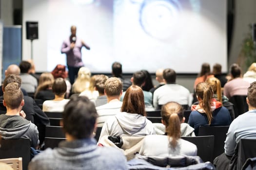 Speaker giving a talk in conference hall at business event. Rear view of unrecognizable people in audience at the conference hall. Business and entrepreneurship concept.