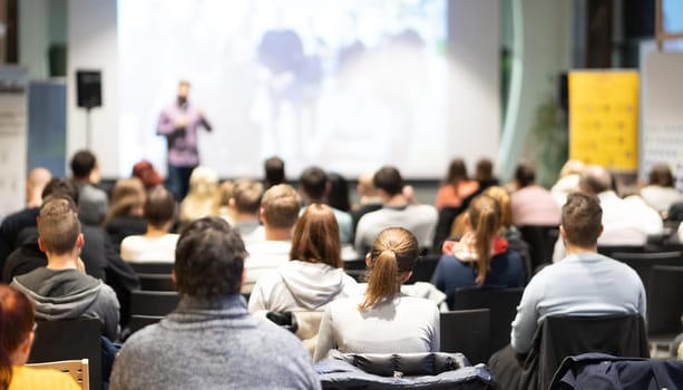 Speaker giving a talk in conference hall at business event. Audience at the conference hall. Business and Entrepreneurship concept. Focus on unrecognizable people in audience.