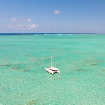 Catamaran sailing boat in turquoise sea lagoon on tropial Mauritius island. Aerial, top down drone view.
